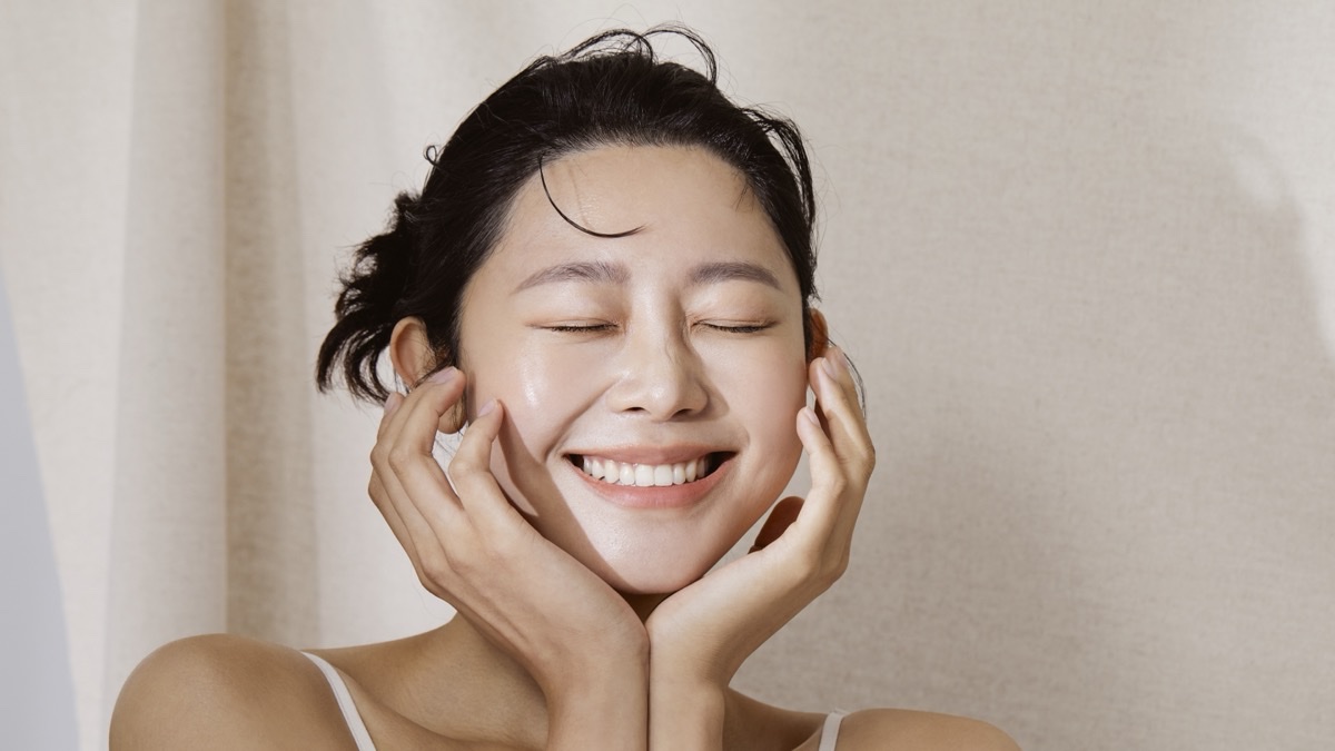 두 손으로 볼을 감싸고 눈을 감은 채 웃는 촉촉한 피부의 여성