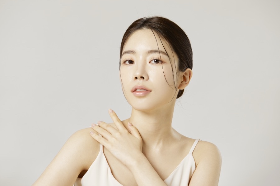 어깨에 손을 얹고 정면을 바라보는 여성의 턱선과 목선이 드러난 뷰티 사진